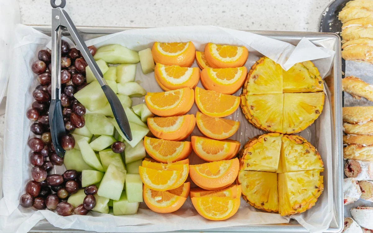 Una bandeja de melón cortado, uvas, naranja y piña con pinzas, dispuesta en un barco