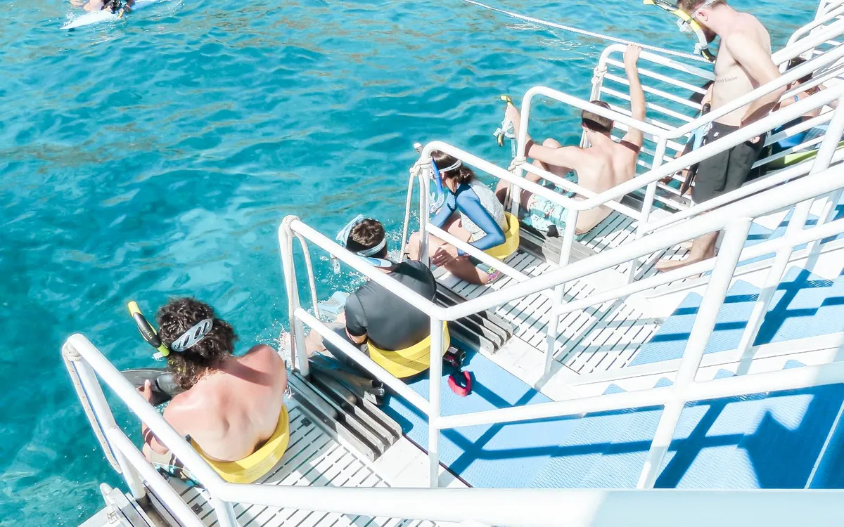 Buceadores con máscara sentados en las escaleras de popa de un catamarán sobre aguas abiertas