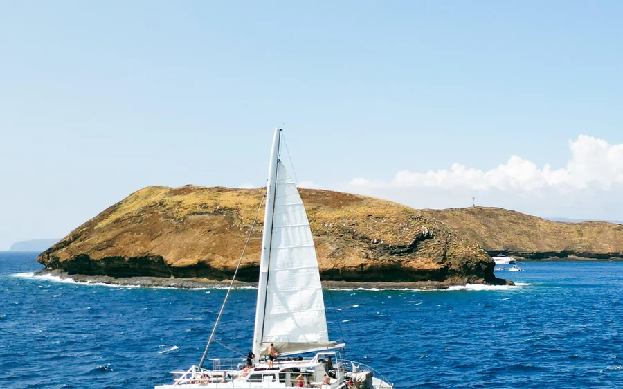 Una vela blanca pasando junto al bajo islote marrón en aguas azules abiertas