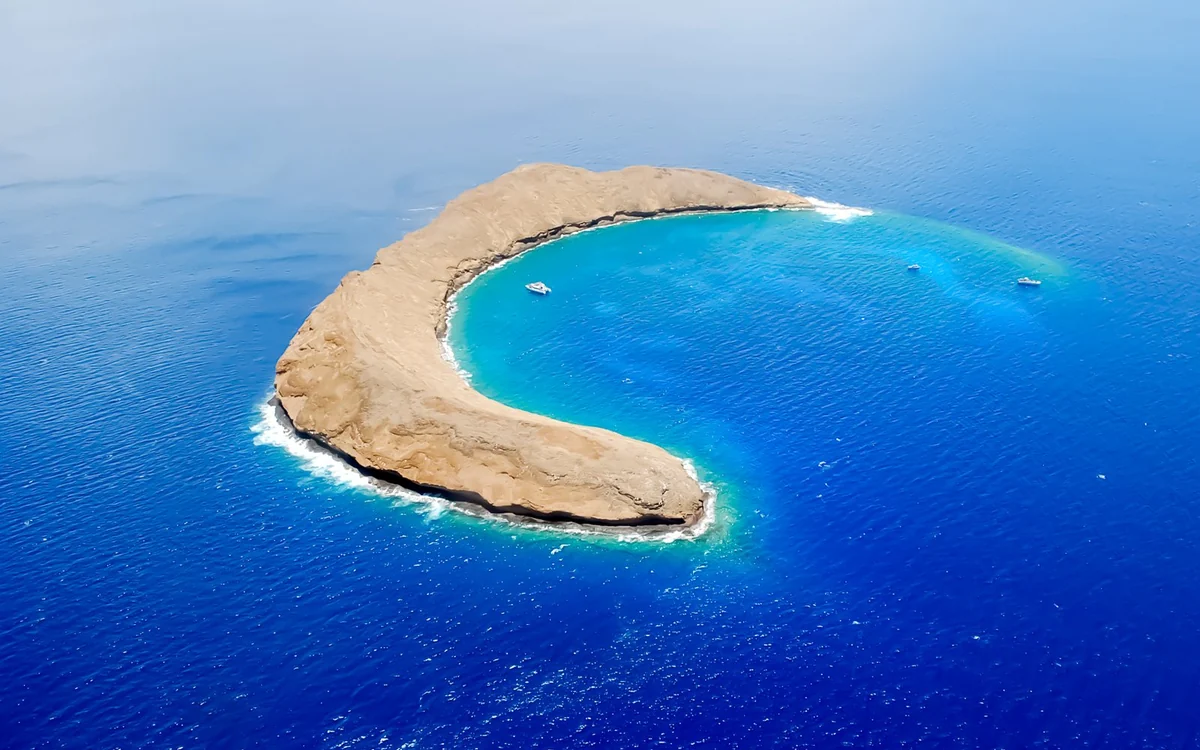 El borde en forma de media luna del cráter Molokini desde el aire, agua turquesa dentro del arco y azul profundo fuera